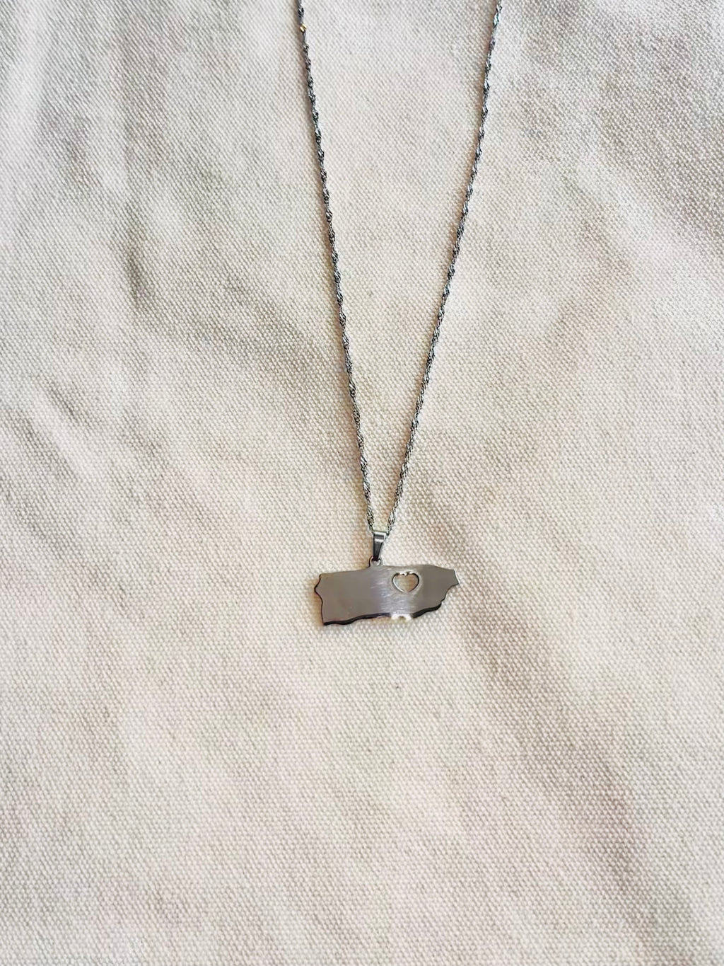 Silver necklace with a pendant on a light gray fabric background