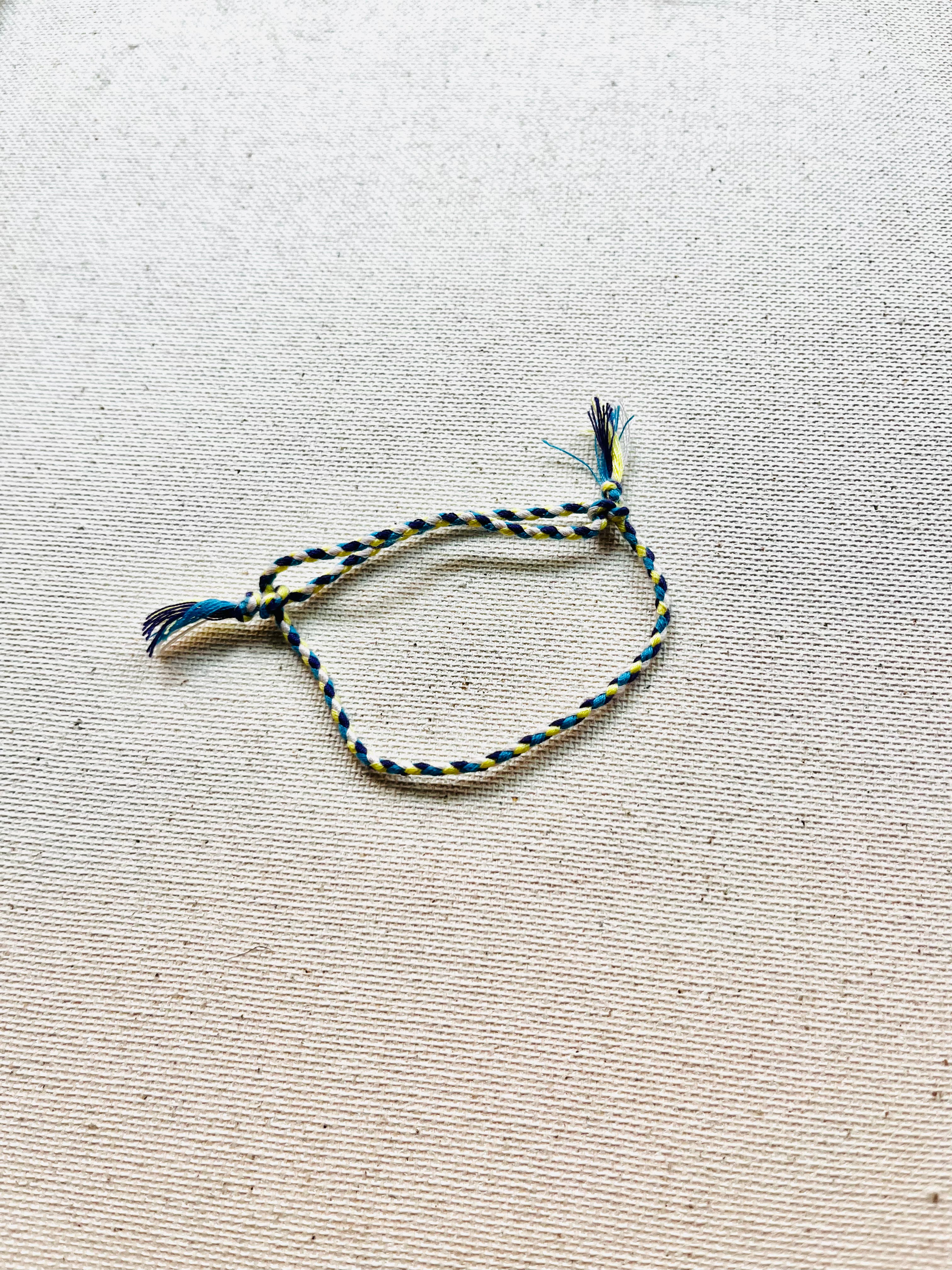 Braided bracelet with blue and yellow threads on a textured beige background
