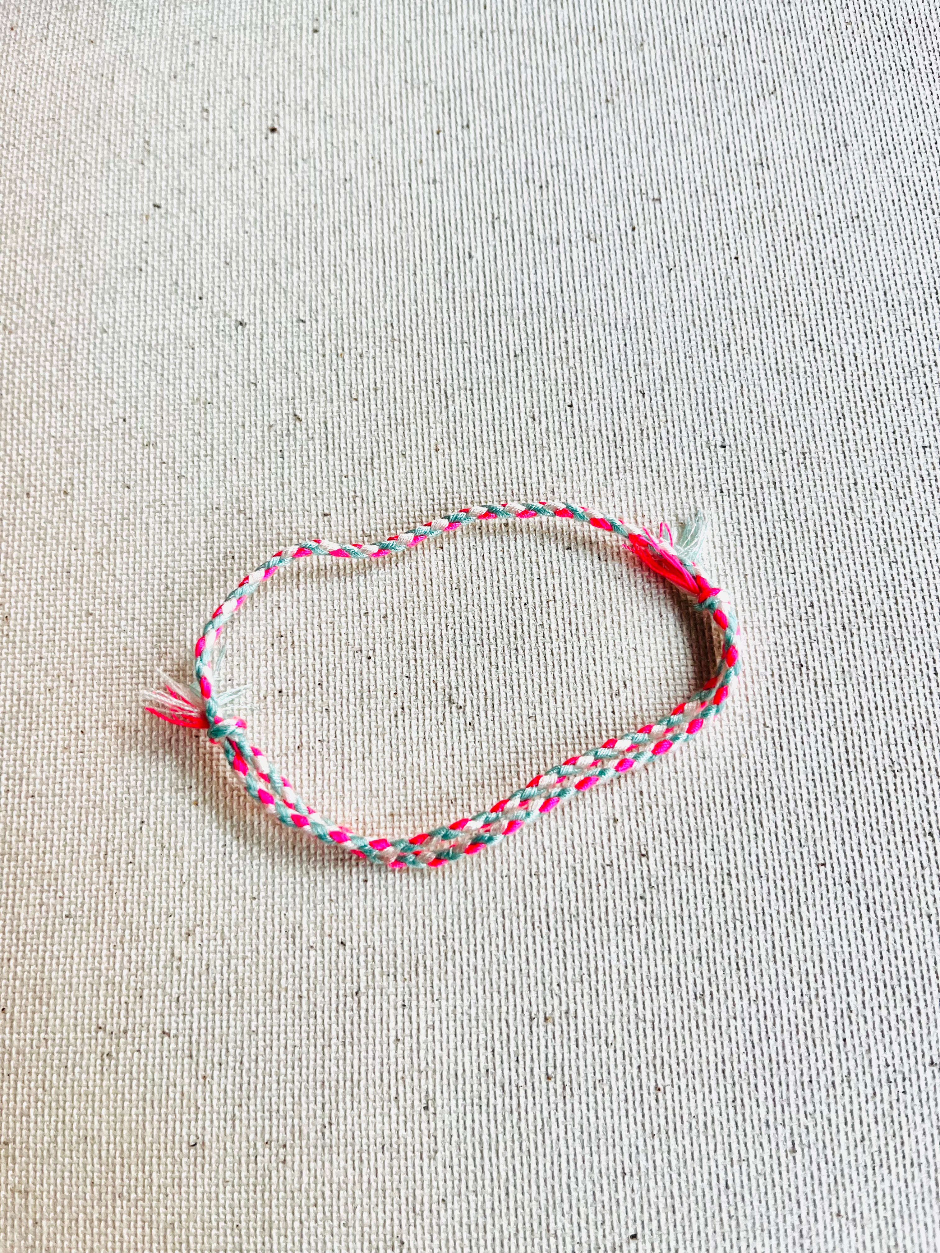 Braided bracelet with pink and red strings on a beige fabric background