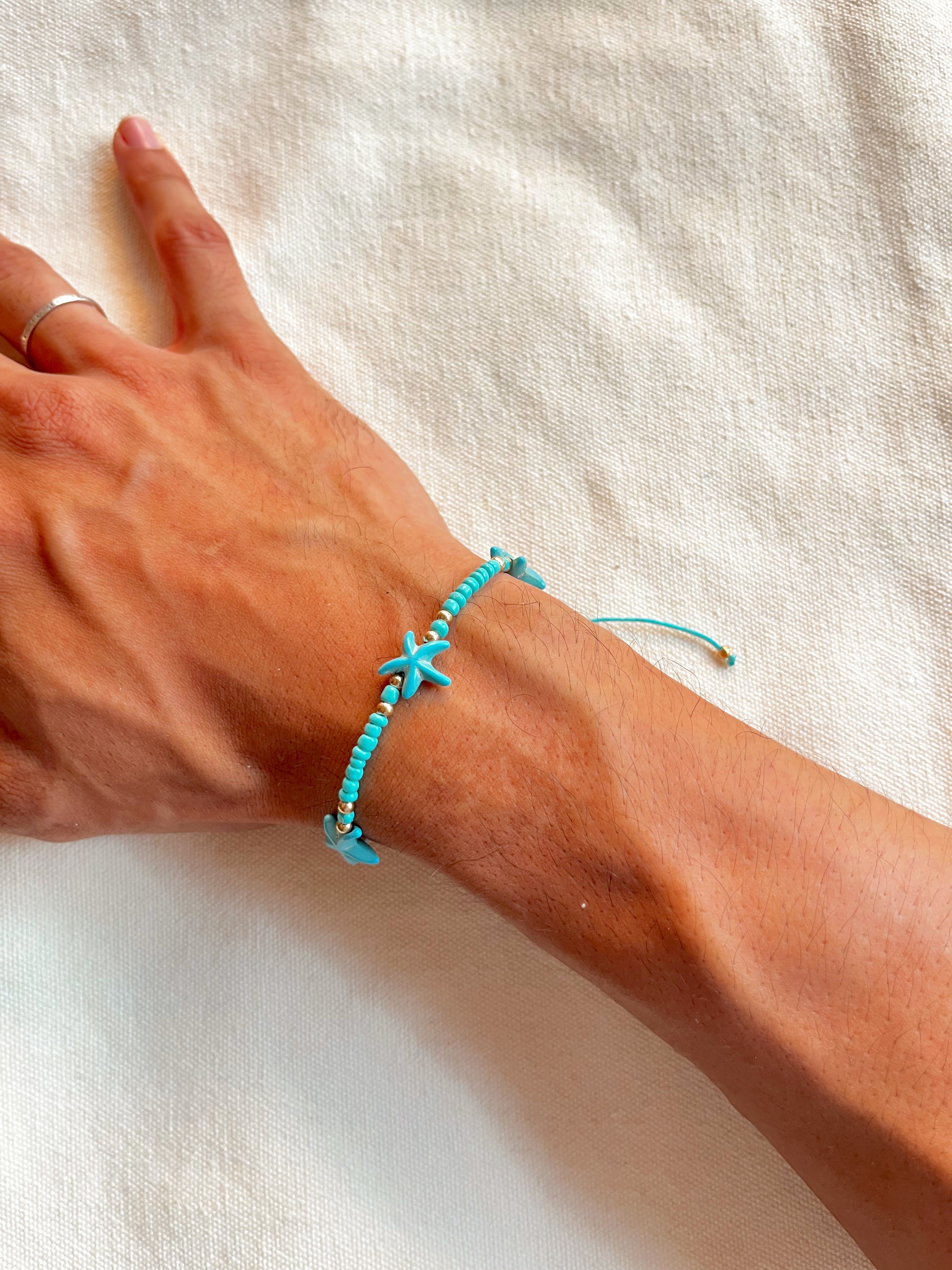 Turquoise starfish bracelet on a wrist against a white background