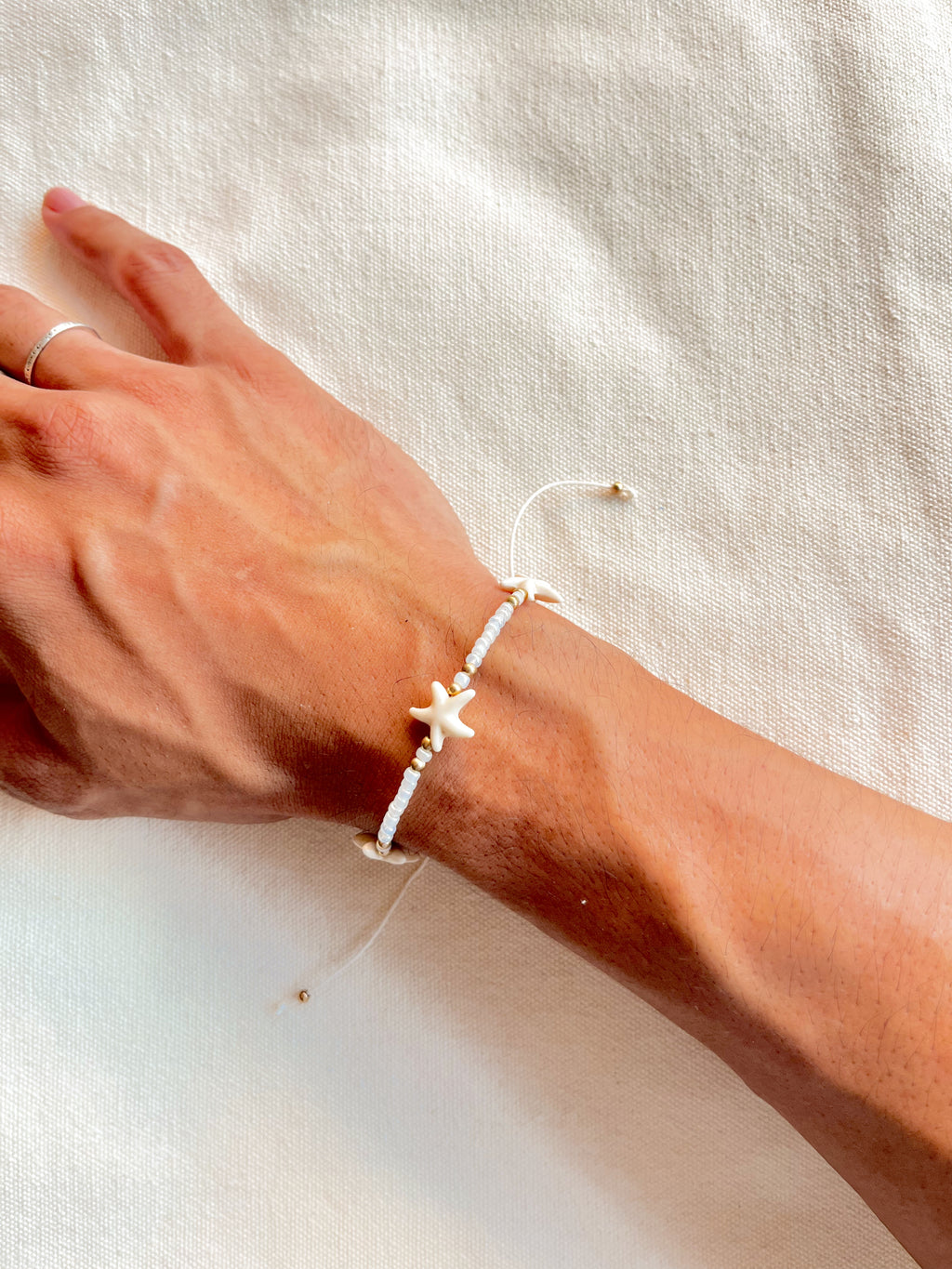 Hand wearing a starfish bracelet on a light fabric background