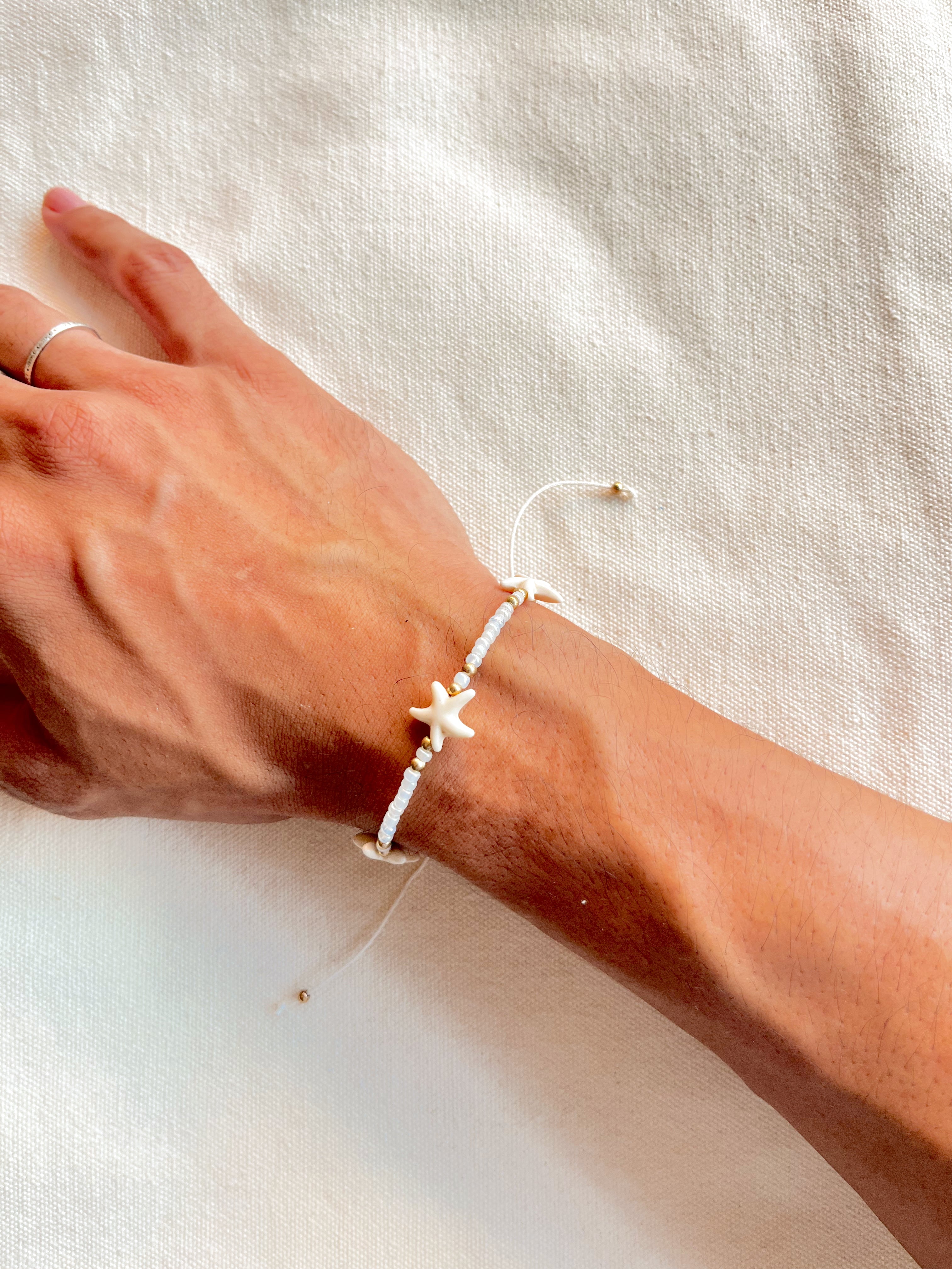 Hand wearing a starfish bracelet on a light fabric background