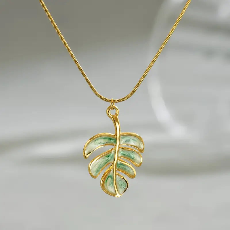 Gold necklace with a green leaf pendant on a light gray background