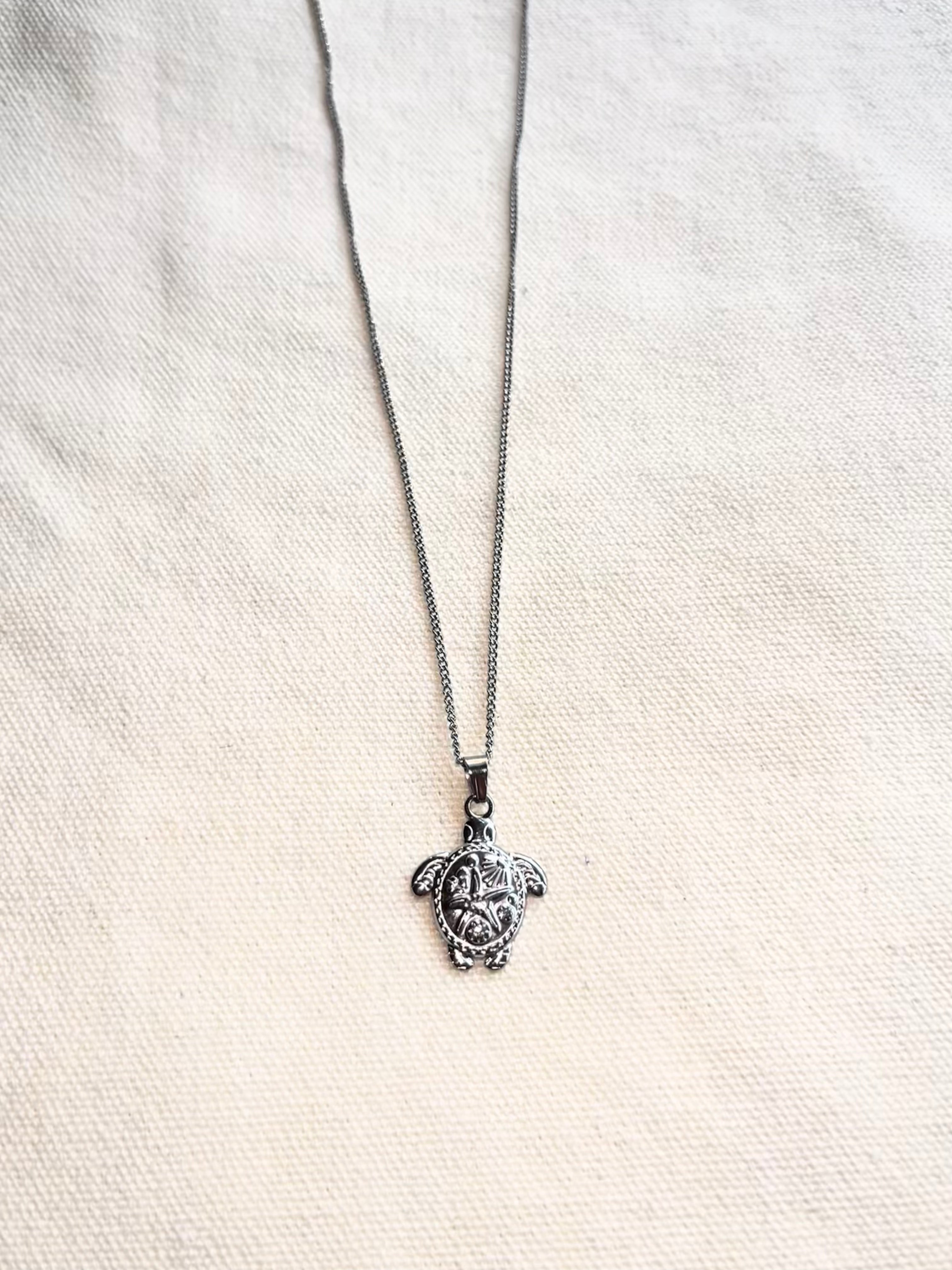 Silver turtle pendant necklace on a white fabric background