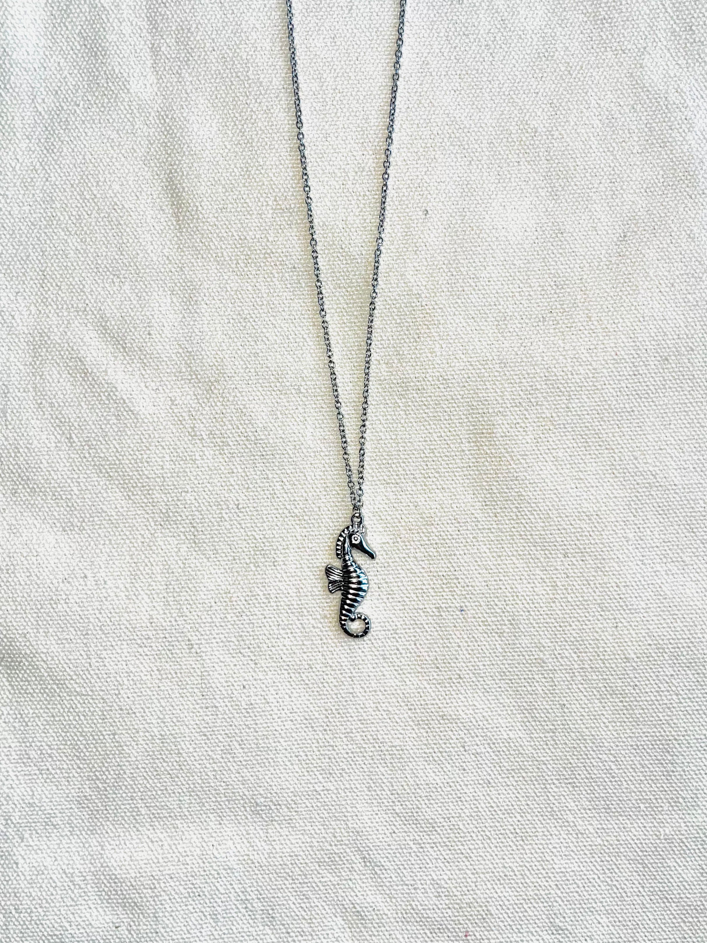 Silver seahorse necklace on a light gray fabric background