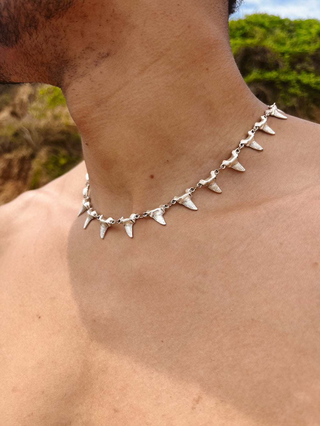 Person wearing a silver necklace with shark tooth pendants outdoors