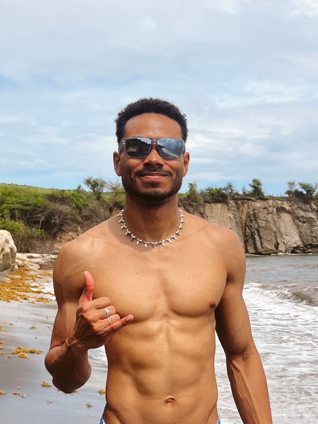 Man with sunglasses and a necklace standing on a beach