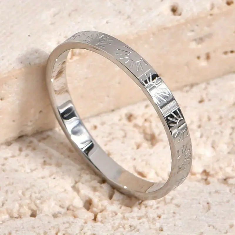 Silver ring with engraved patterns on a sandy background