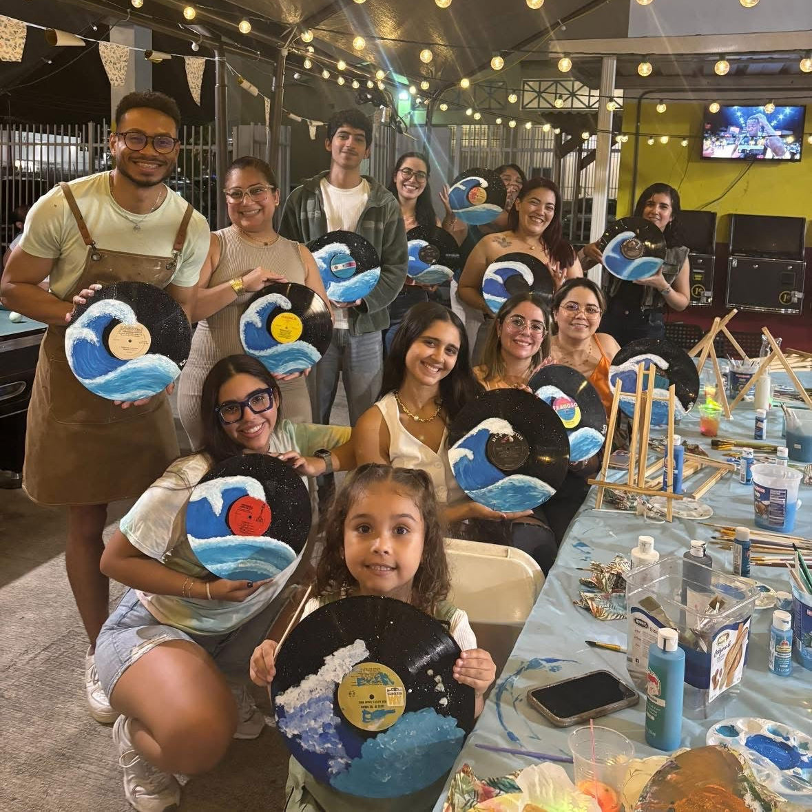Group of people, including children, holding vinyls with artistic designs in a workshop setting.