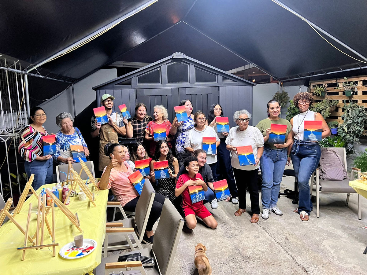 Group of people holding colorful paintings in a backyard setting