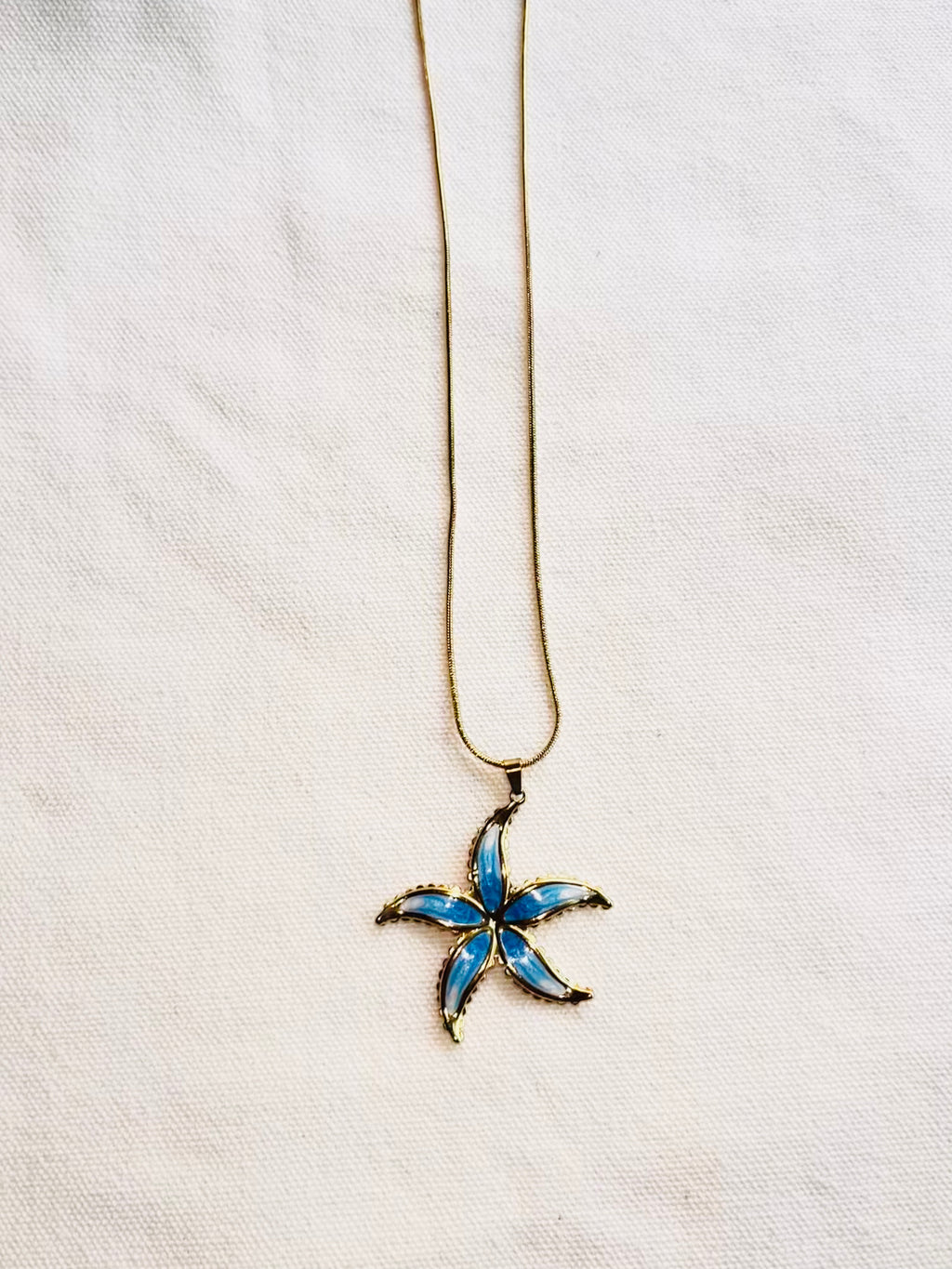 Starfish-shaped pendant on a chain against a white fabric background