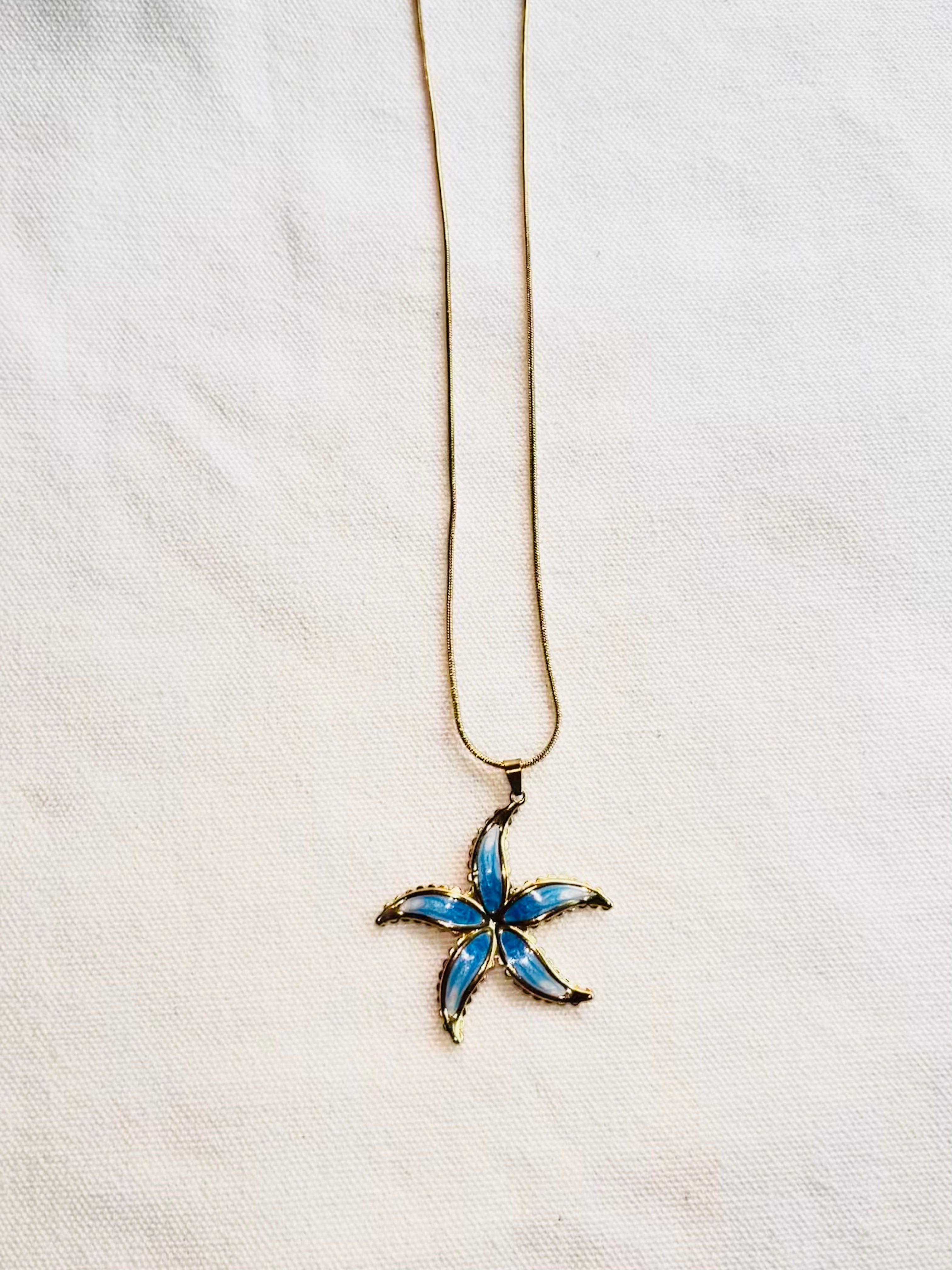 Starfish-shaped pendant on a chain against a white fabric background