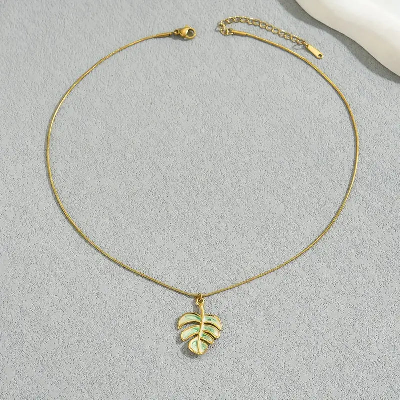 Gold necklace with a leaf-shaped pendant on a light gray background